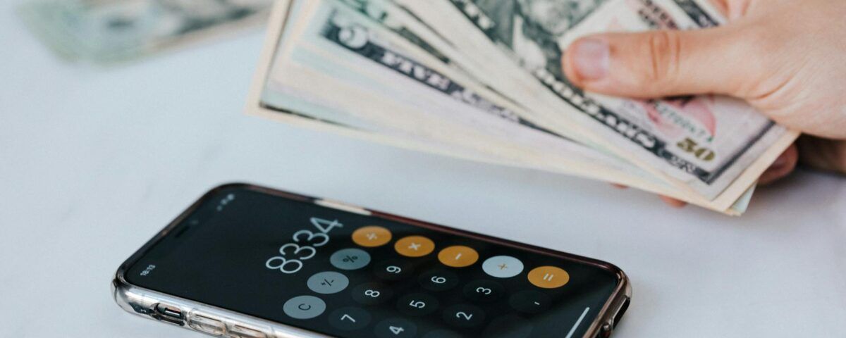 crop faceless person with cash and calculator app on smartphone