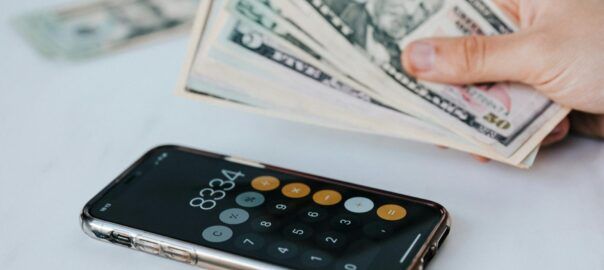 crop faceless person with cash and calculator app on smartphone